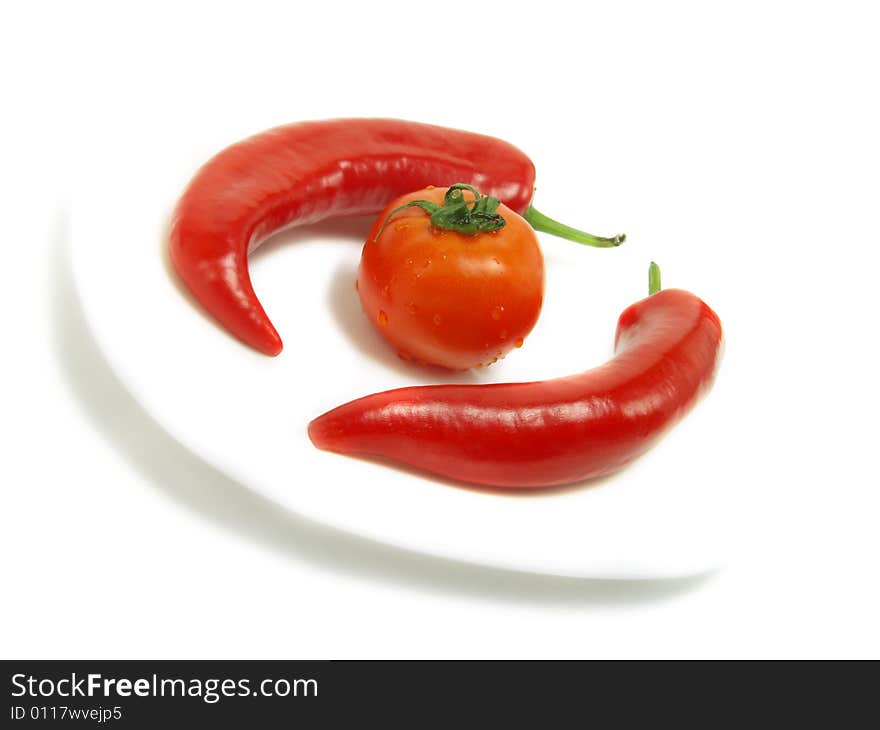 Two fresh chili peppers and a ripe tomato on a white plate and isolated on white background. Two fresh chili peppers and a ripe tomato on a white plate and isolated on white background