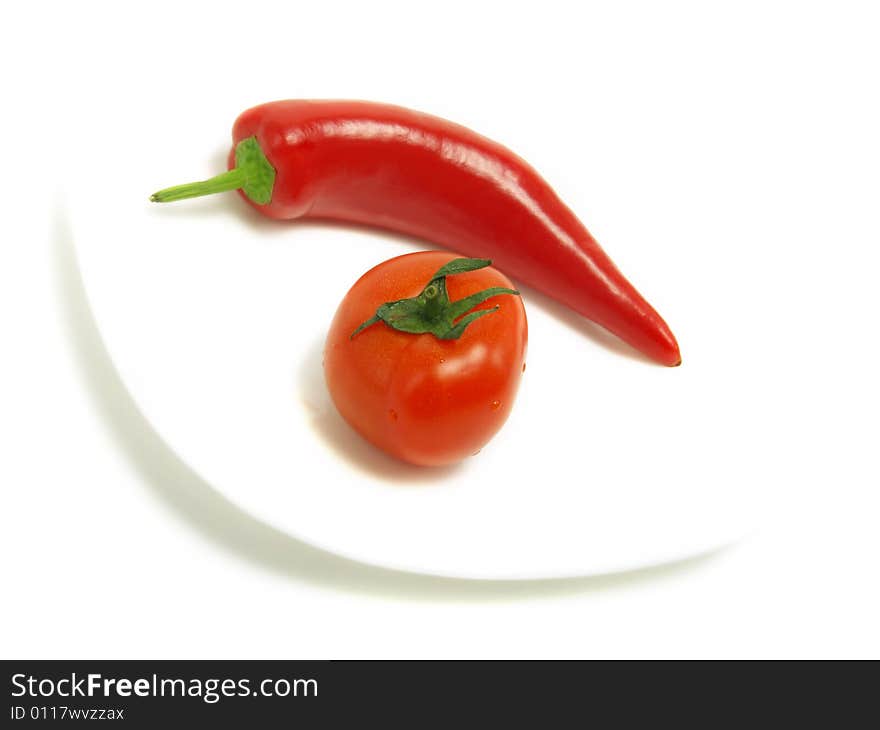 A fresh tomato and a blurred ripe chili pepper on a white plate and isolated on white background. A fresh tomato and a blurred ripe chili pepper on a white plate and isolated on white background