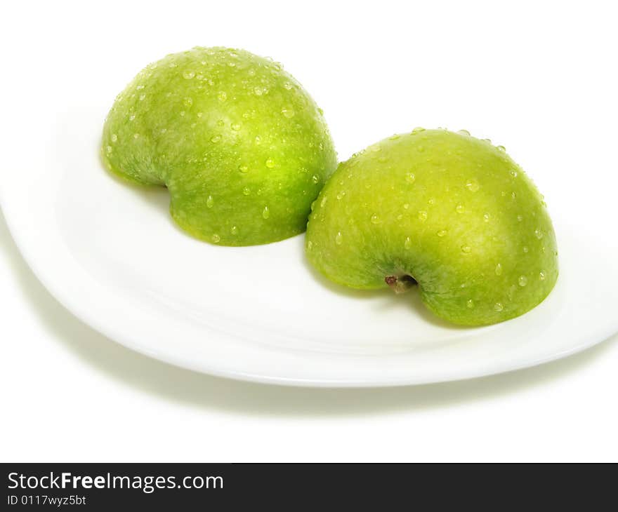 Two half parts of a fresh ripe green apple with water drops on white plate and isolated on white background. Two half parts of a fresh ripe green apple with water drops on white plate and isolated on white background