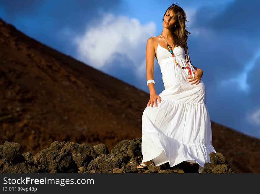 Young model with white dress on volcanic lava rocks. Young model with white dress on volcanic lava rocks