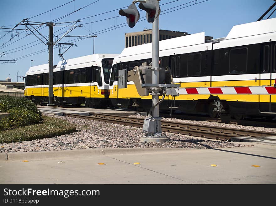 A light rail or cable cars speeding past an activated crossing guardrail. A light rail or cable cars speeding past an activated crossing guardrail.