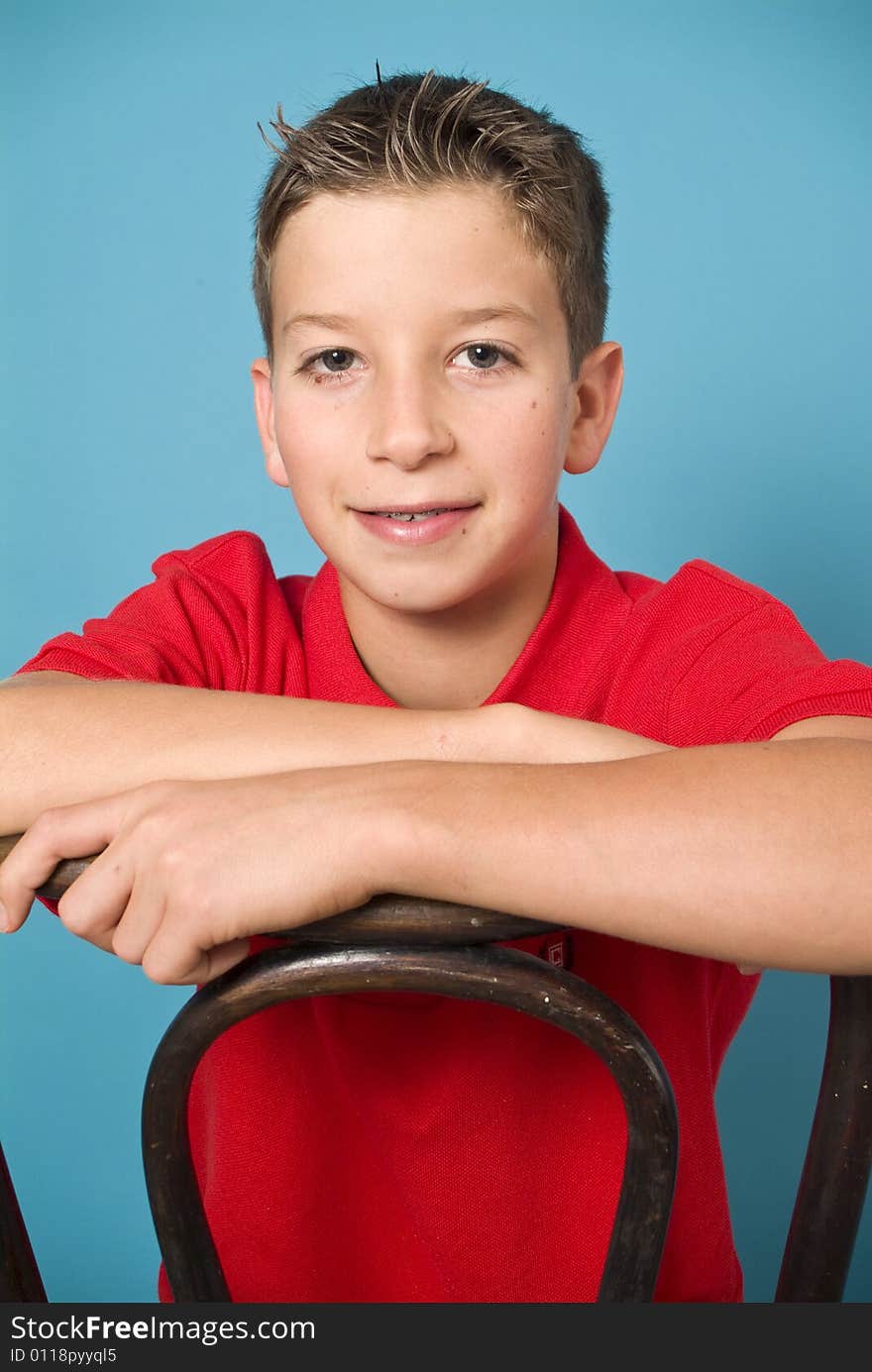 A clean cut young man in a red shirt straddling an old bentwood back chair.