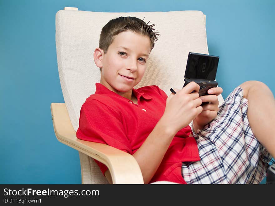 A boy relaxed in a chair holding a video game device. A boy relaxed in a chair holding a video game device.