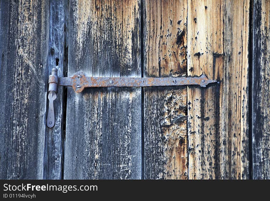 A close up of an old rusted metal hinge on a weathered unpainted door. A close up of an old rusted metal hinge on a weathered unpainted door.