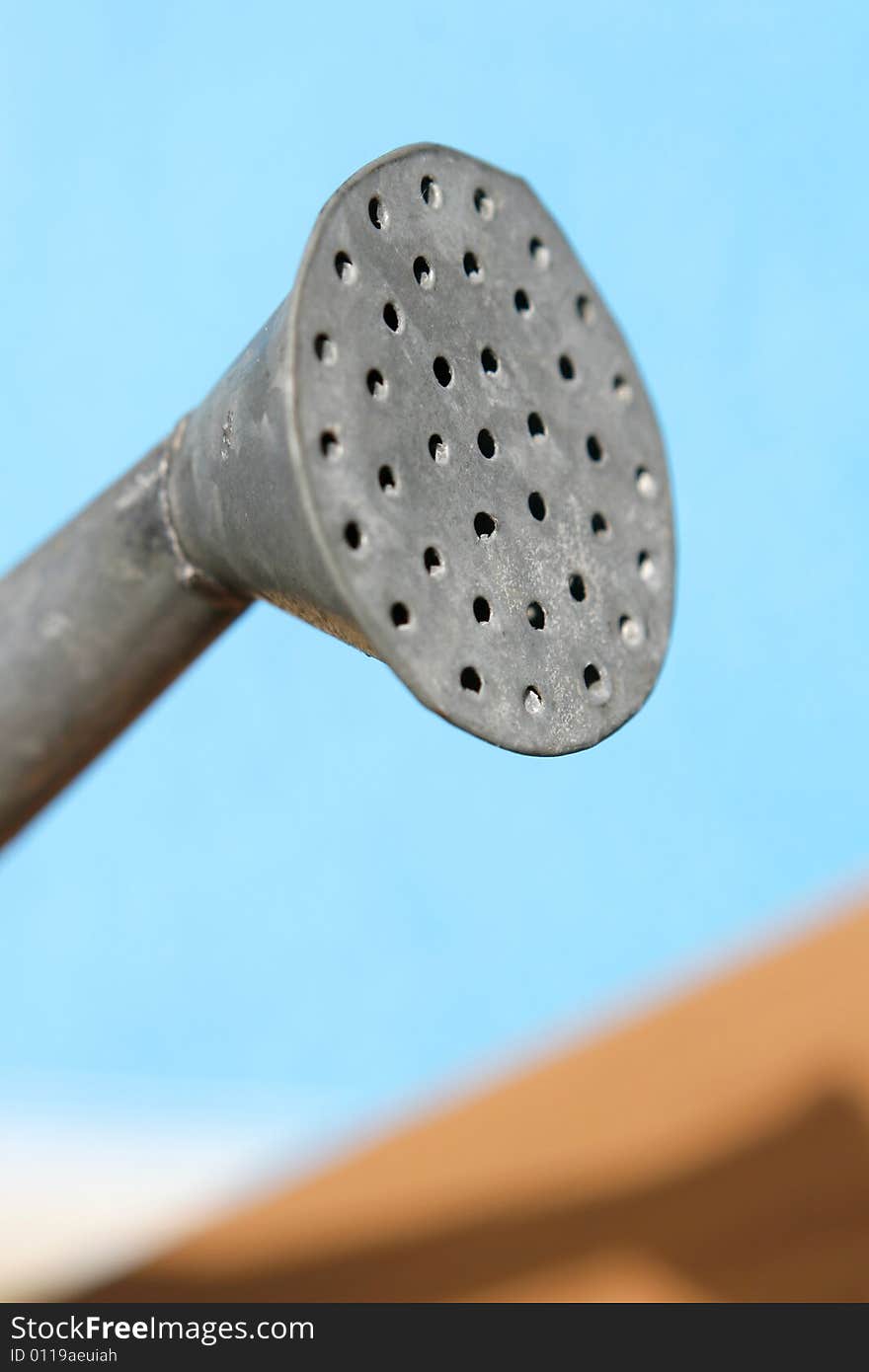 Closeup, abstract shot of an aluminum watering can spout.  The background is blue.