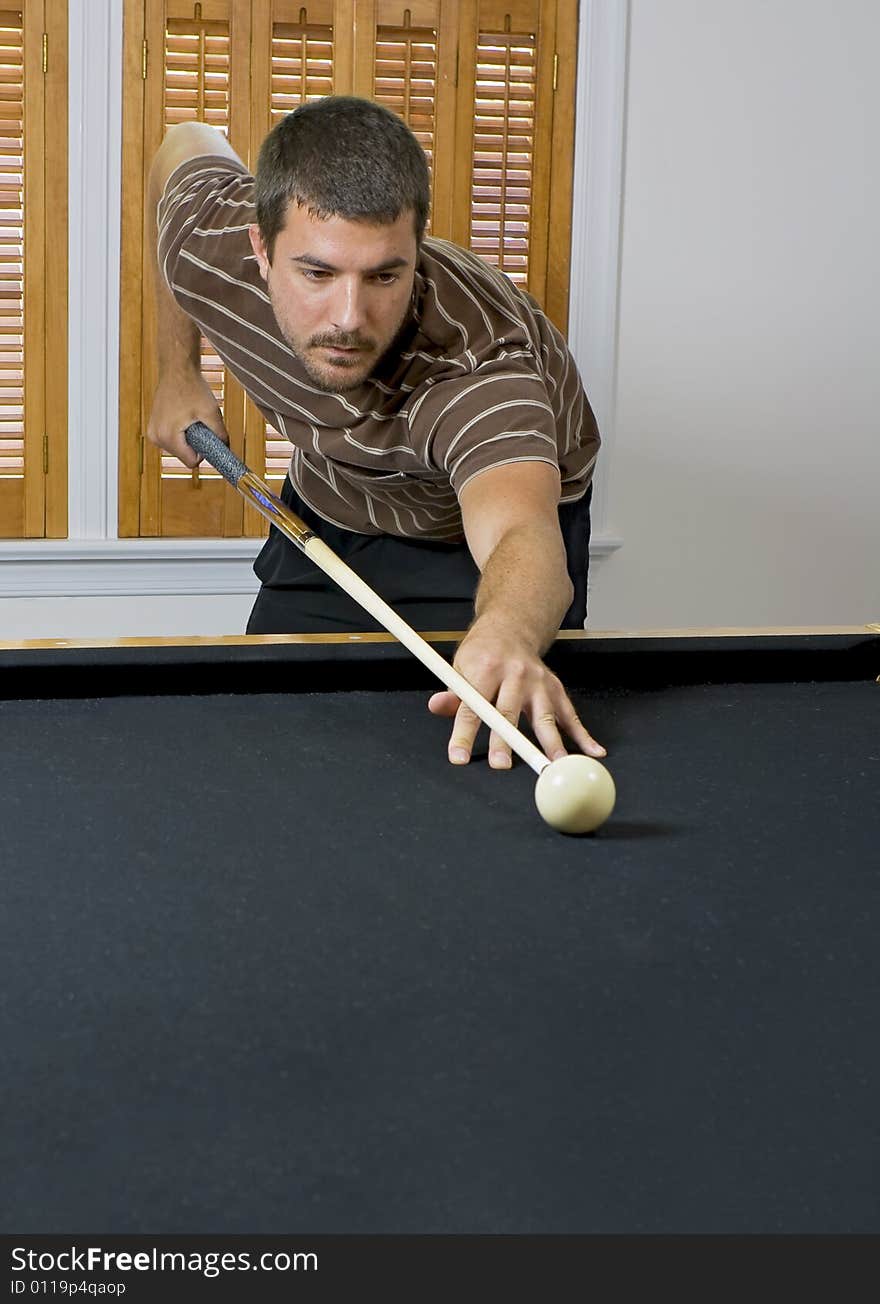 Young man lining up the cue ball, getting ready to break the billiards on the other end of the table. Young man lining up the cue ball, getting ready to break the billiards on the other end of the table.