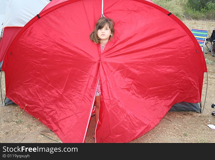 Young girl peeking her head out of a red tent. Young girl peeking her head out of a red tent.