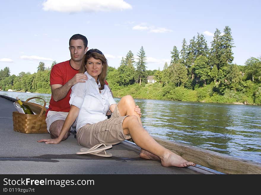 Couple sitting together by a lake with a picnic basket. Horizontally framed photograph. Couple sitting together by a lake with a picnic basket. Horizontally framed photograph