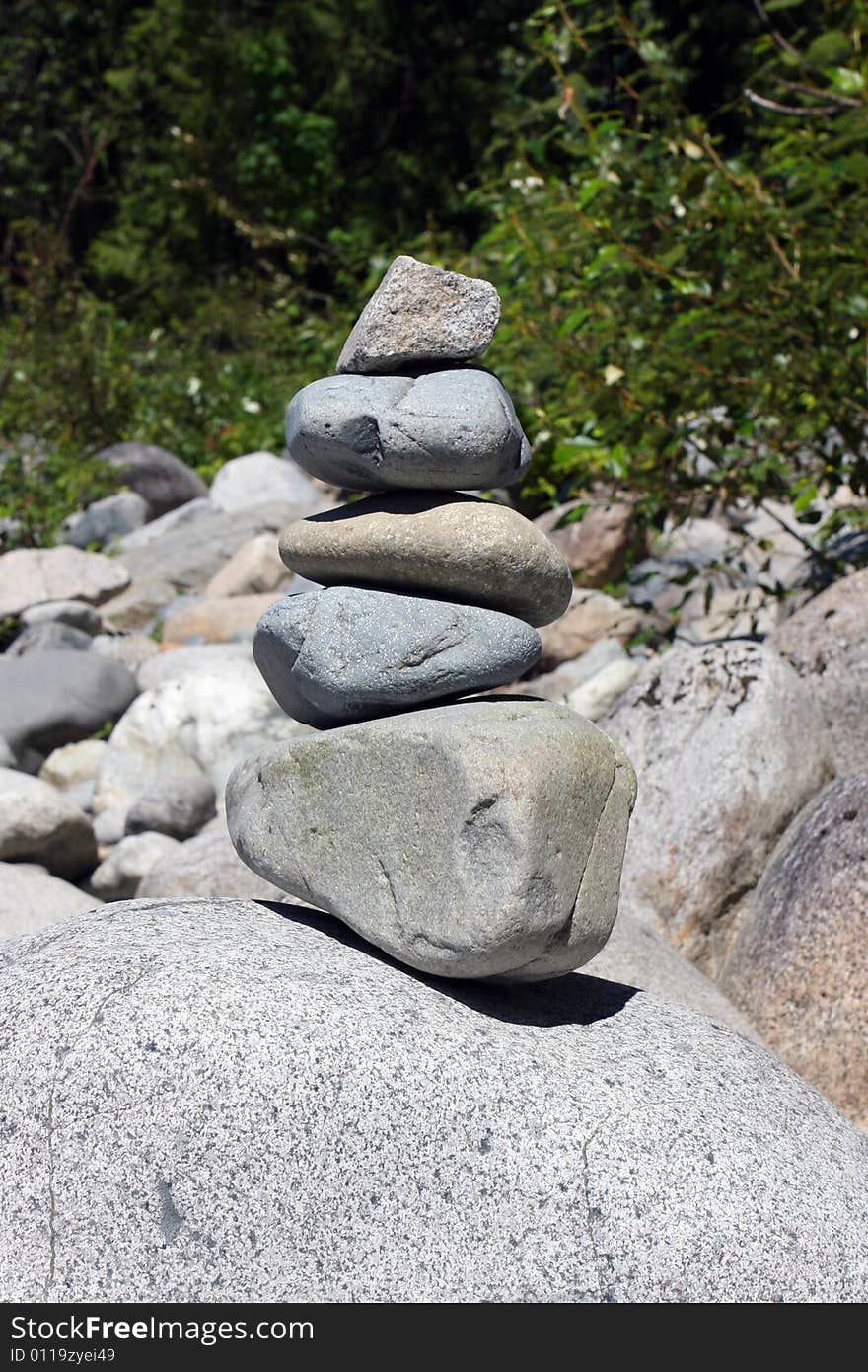 Five various sized rocks stacked and balanced on a large boulder. Five various sized rocks stacked and balanced on a large boulder.