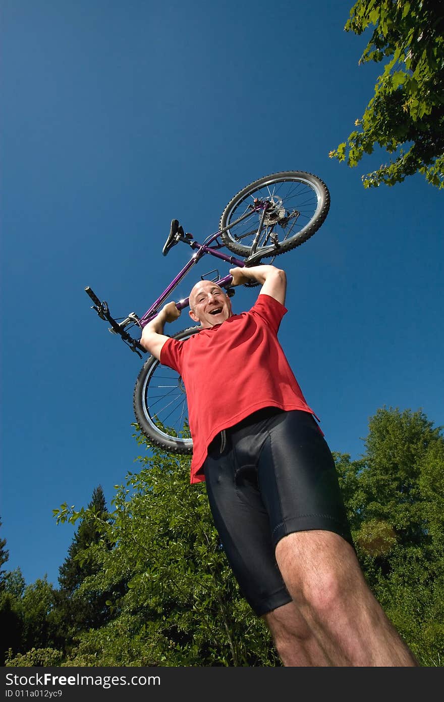 A man lifting a bicycle high over his head on a sunny day, at a park. - vertically framed. A man lifting a bicycle high over his head on a sunny day, at a park. - vertically framed