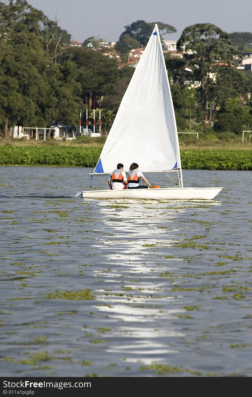 A young couple is sailing on a lake together.  They are looking away from the camera.  Vertically framed shot. A young couple is sailing on a lake together.  They are looking away from the camera.  Vertically framed shot.