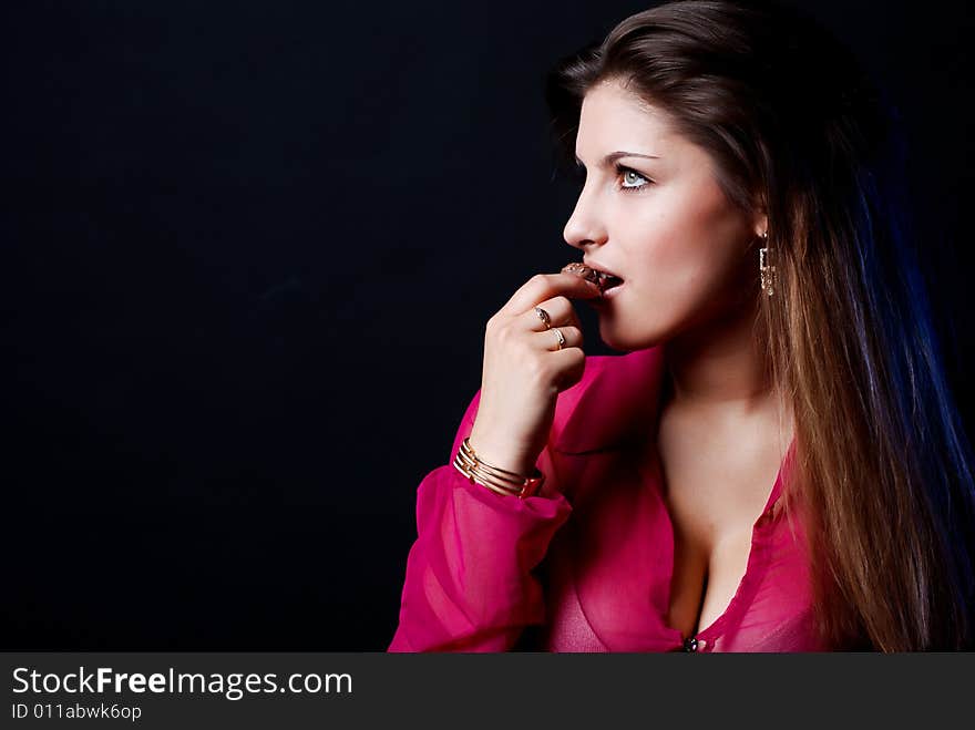 Portrait of beautiful girl in a pink woman's jacket with a chocolate candy in the mouth