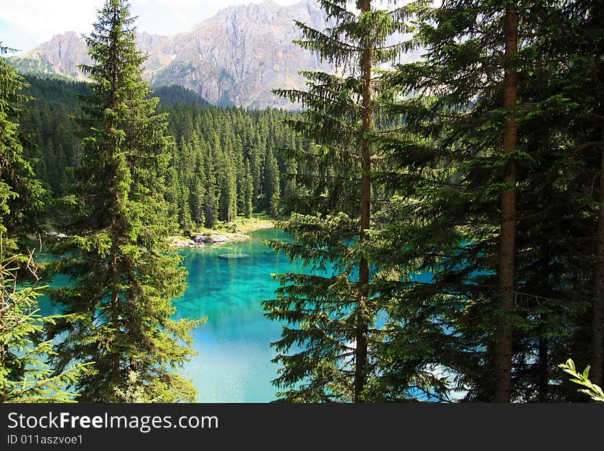 Sella montain group, and Carezza lake's turquoise colorful water.  Green pines forest on blue lake water. Italy. Sella montain group, and Carezza lake's turquoise colorful water.  Green pines forest on blue lake water. Italy