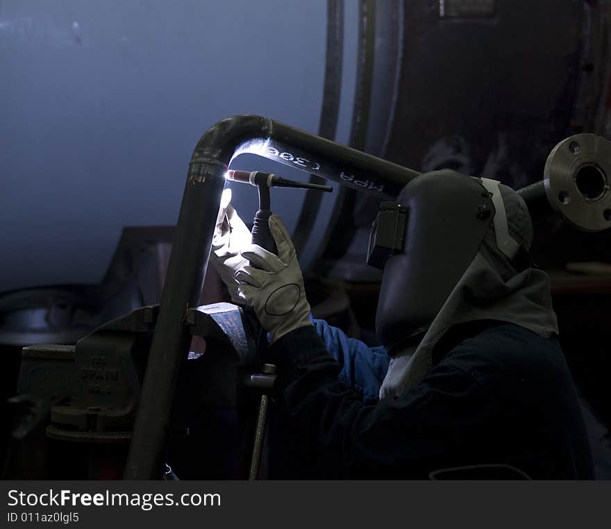 Welder working on steel pipes in an industrial workshop. dark, contrasty photo.