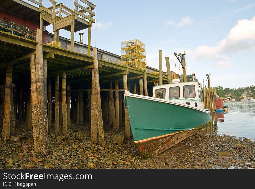 A view of a Maine lobster boat aground at low tide next to a large wooden wharf or pier. A view of a Maine lobster boat aground at low tide next to a large wooden wharf or pier.