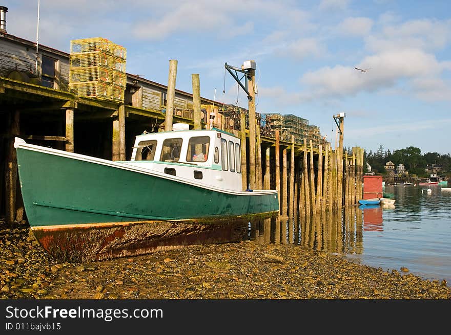 A view of a Maine lobster boat grounded at low tide next to a large wooden wharf or pier. A view of a Maine lobster boat grounded at low tide next to a large wooden wharf or pier.