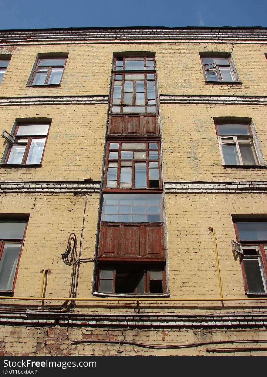 The old multi-storey apartment house from a brick is painted light yellow color with greater glass windows on a background of the dark blue sky. The old multi-storey apartment house from a brick is painted light yellow color with greater glass windows on a background of the dark blue sky