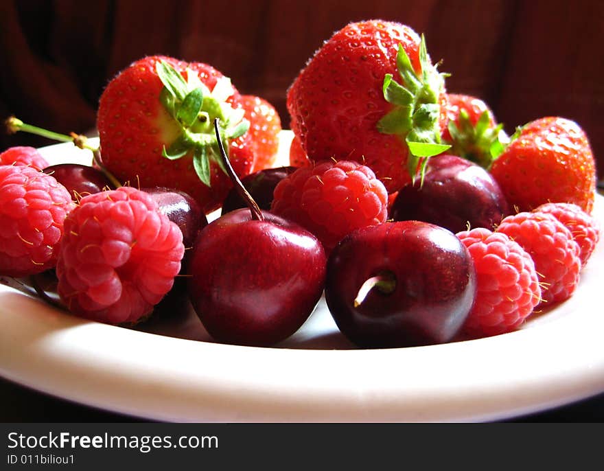 A white plate of red summer fruits - strawberries, cherries and raspberries. A white plate of red summer fruits - strawberries, cherries and raspberries.