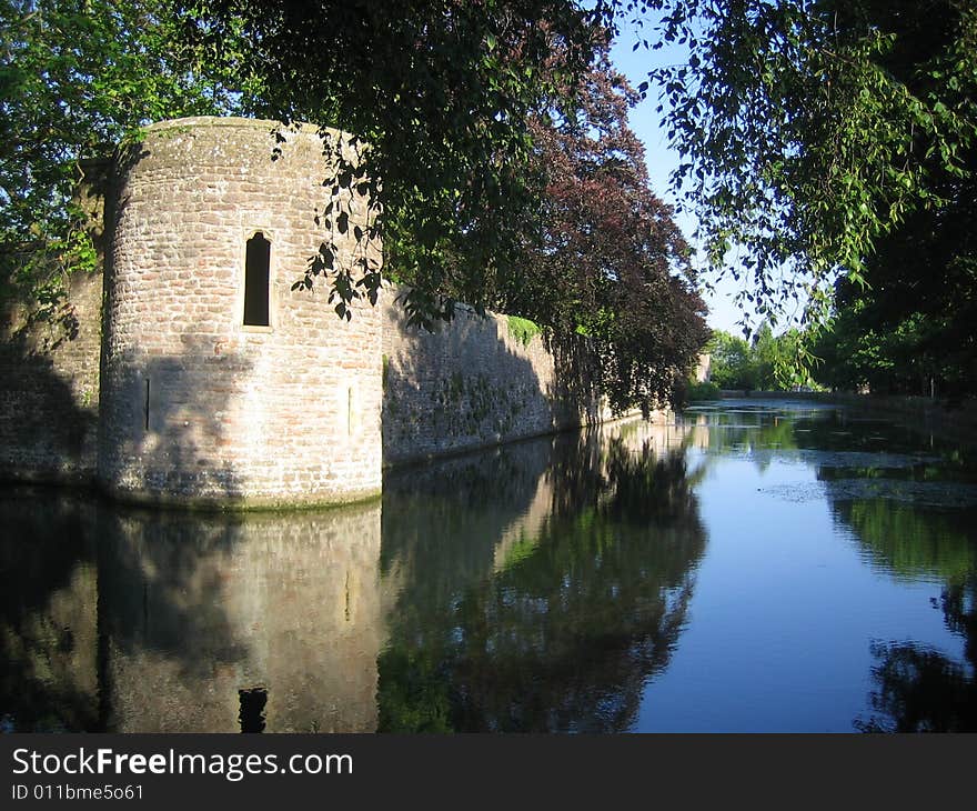 A tree framed image of a stone wall and tower reflected in surrounding water. A tree framed image of a stone wall and tower reflected in surrounding water.