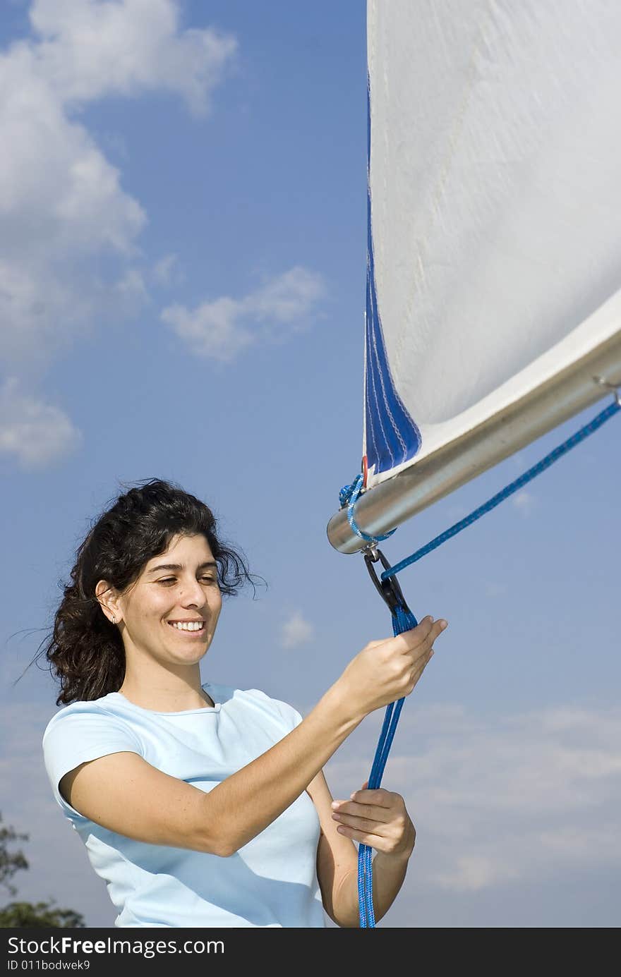 Woman standing next to sailboat tying rigging to sail. Vertically framed photo. Woman standing next to sailboat tying rigging to sail. Vertically framed photo