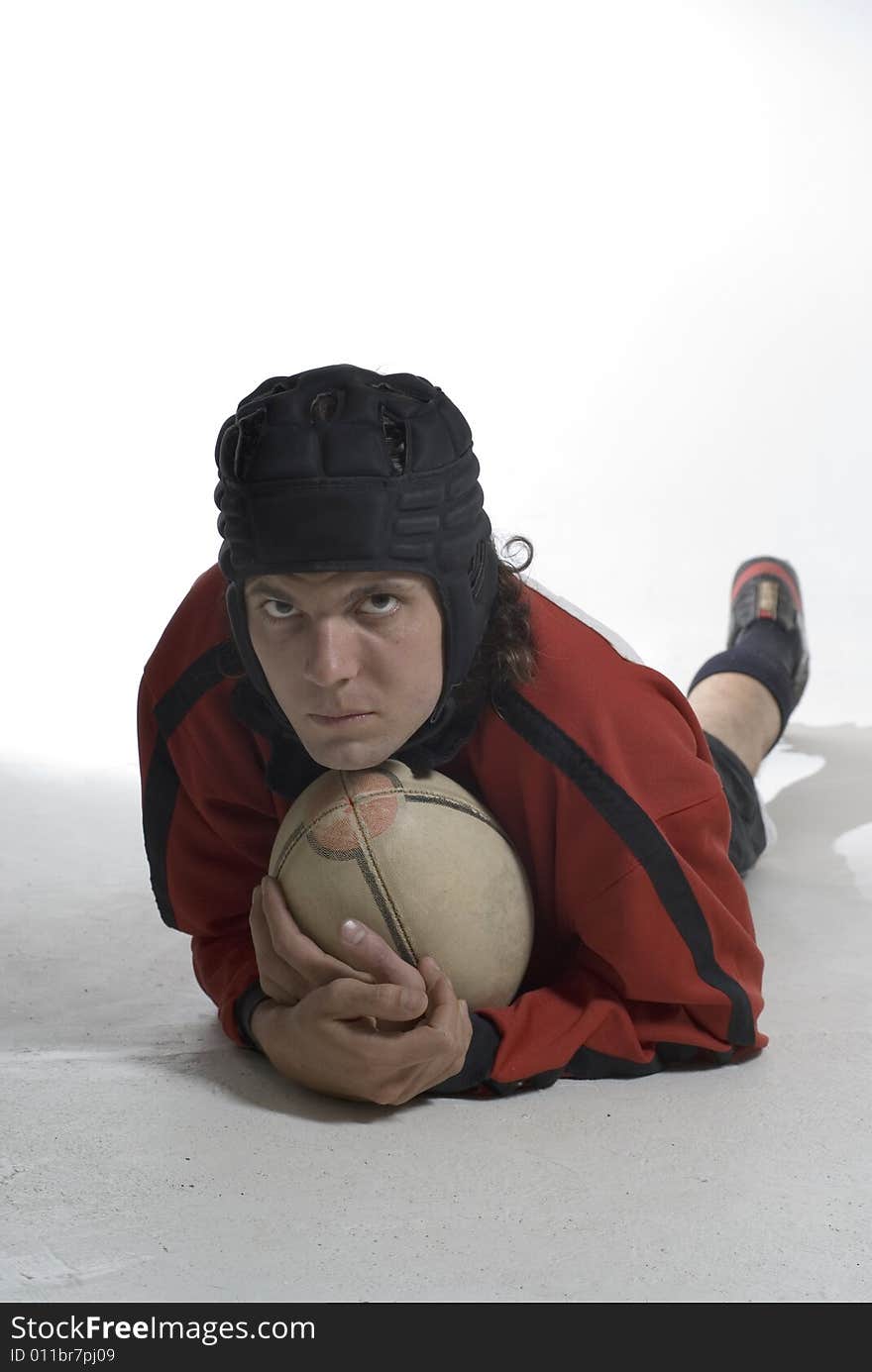 A young man, lies on the ground, holding a rugby ball, looking serious. Vertically framed shot. A young man, lies on the ground, holding a rugby ball, looking serious. Vertically framed shot.