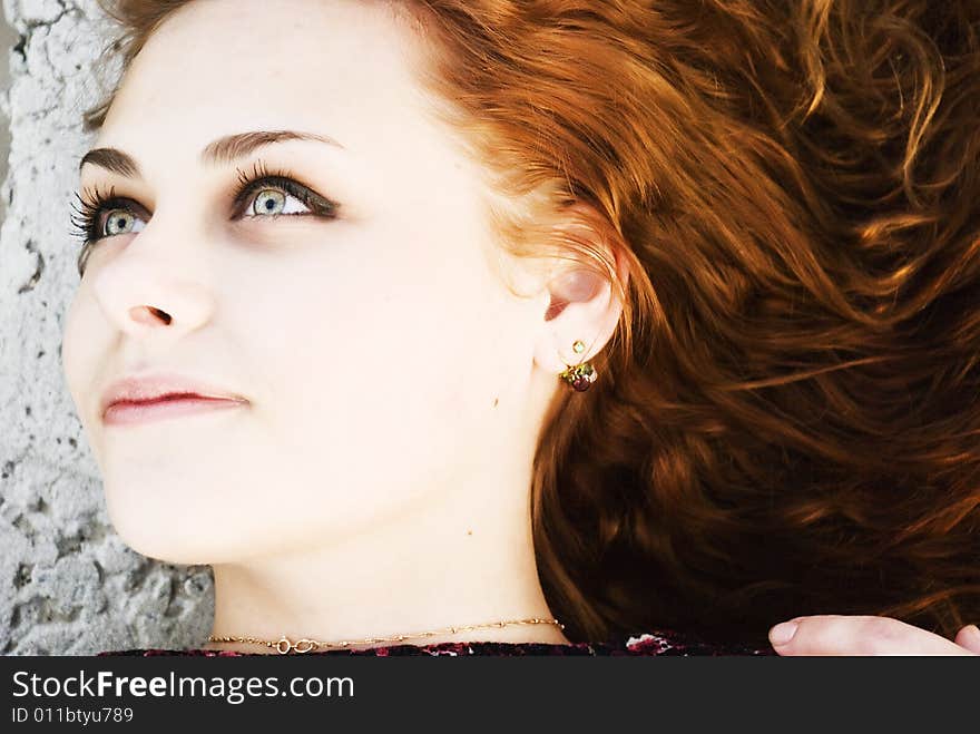 Face of beautiful redheaded girl of looking aside, on a background a stone wall. Face of beautiful redheaded girl of looking aside, on a background a stone wall