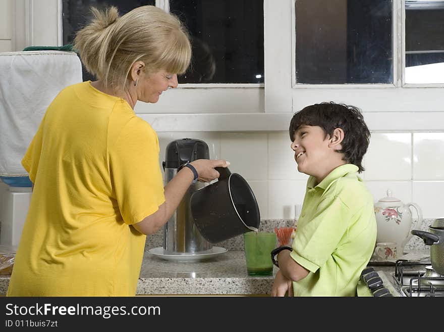 Woman and boy standing in kitchen. Woman pouring boy drink. Boy smiling at woman. Horizontally framed photo. Woman and boy standing in kitchen. Woman pouring boy drink. Boy smiling at woman. Horizontally framed photo.