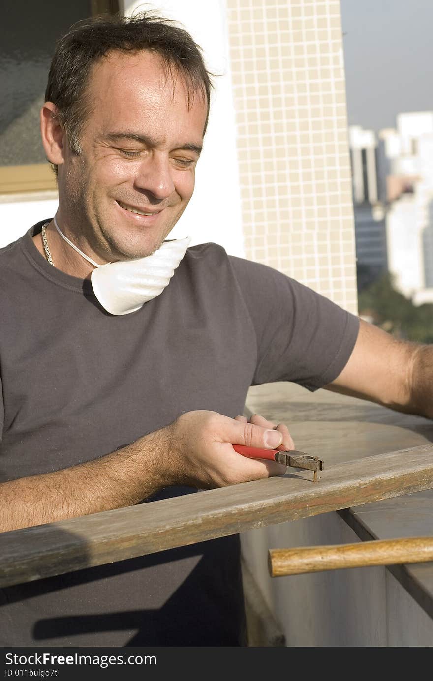 Man pulling nail with pliers. He is smiling and looking at the nail. He has a mask around his neck. Vertically framed shot. Man pulling nail with pliers. He is smiling and looking at the nail. He has a mask around his neck. Vertically framed shot.