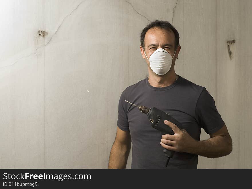 Man standing while holding drill. He is wearing a mask and smiling. He is looking at cameral. Horizontally framed shot. Man standing while holding drill. He is wearing a mask and smiling. He is looking at cameral. Horizontally framed shot.