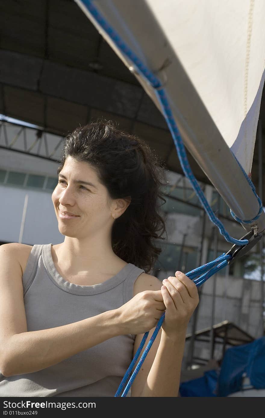 Woman standing next to sailboat smiling away from camera and holding sail rigging. Vertically framed photo. Woman standing next to sailboat smiling away from camera and holding sail rigging. Vertically framed photo.