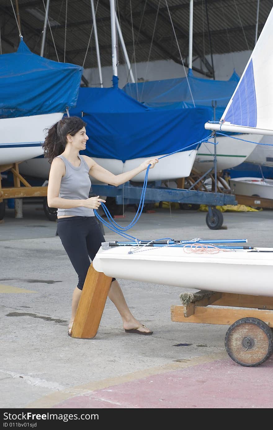 Woman standing behind sailboat on trailer. Tightening sail rigging. Vertically framed photo. Woman standing behind sailboat on trailer. Tightening sail rigging. Vertically framed photo