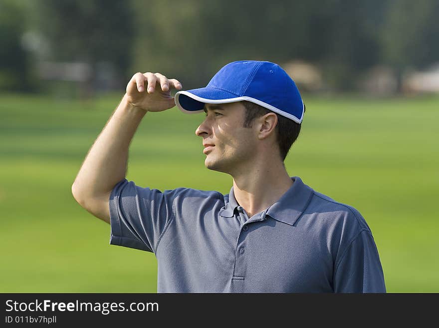 Man's profile while standing on golf course shielding eyes from sun - Horizontally framed photo. Man's profile while standing on golf course shielding eyes from sun - Horizontally framed photo
