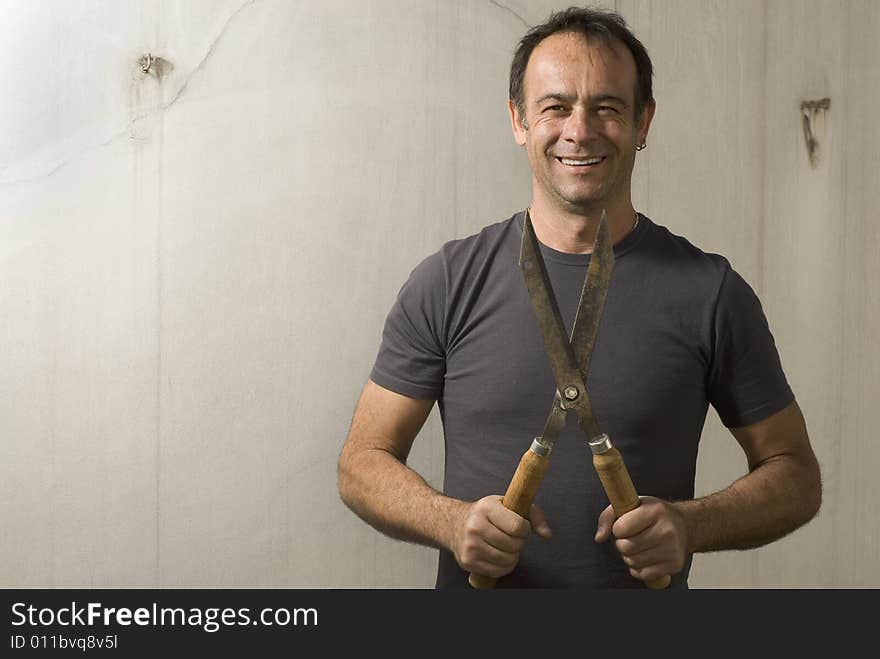 Man standing smiling at camera holding pair of garden shears. Horizontally framed shot. Man standing smiling at camera holding pair of garden shears. Horizontally framed shot.