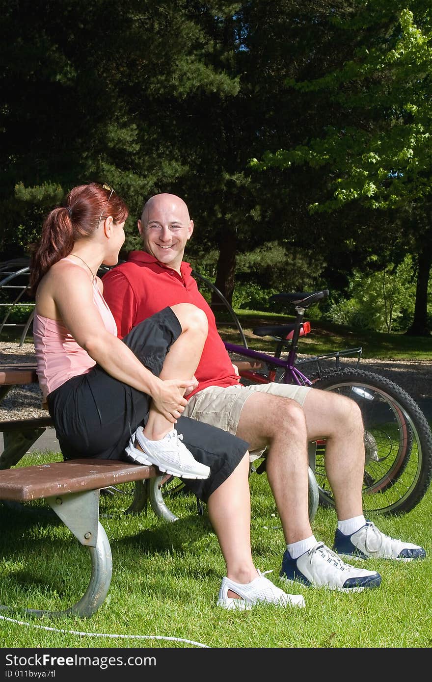 Happy couple sitting on a park bench next to their bicycles. They are looking at each other and smiling. Vertically framed photograph. Happy couple sitting on a park bench next to their bicycles. They are looking at each other and smiling. Vertically framed photograph