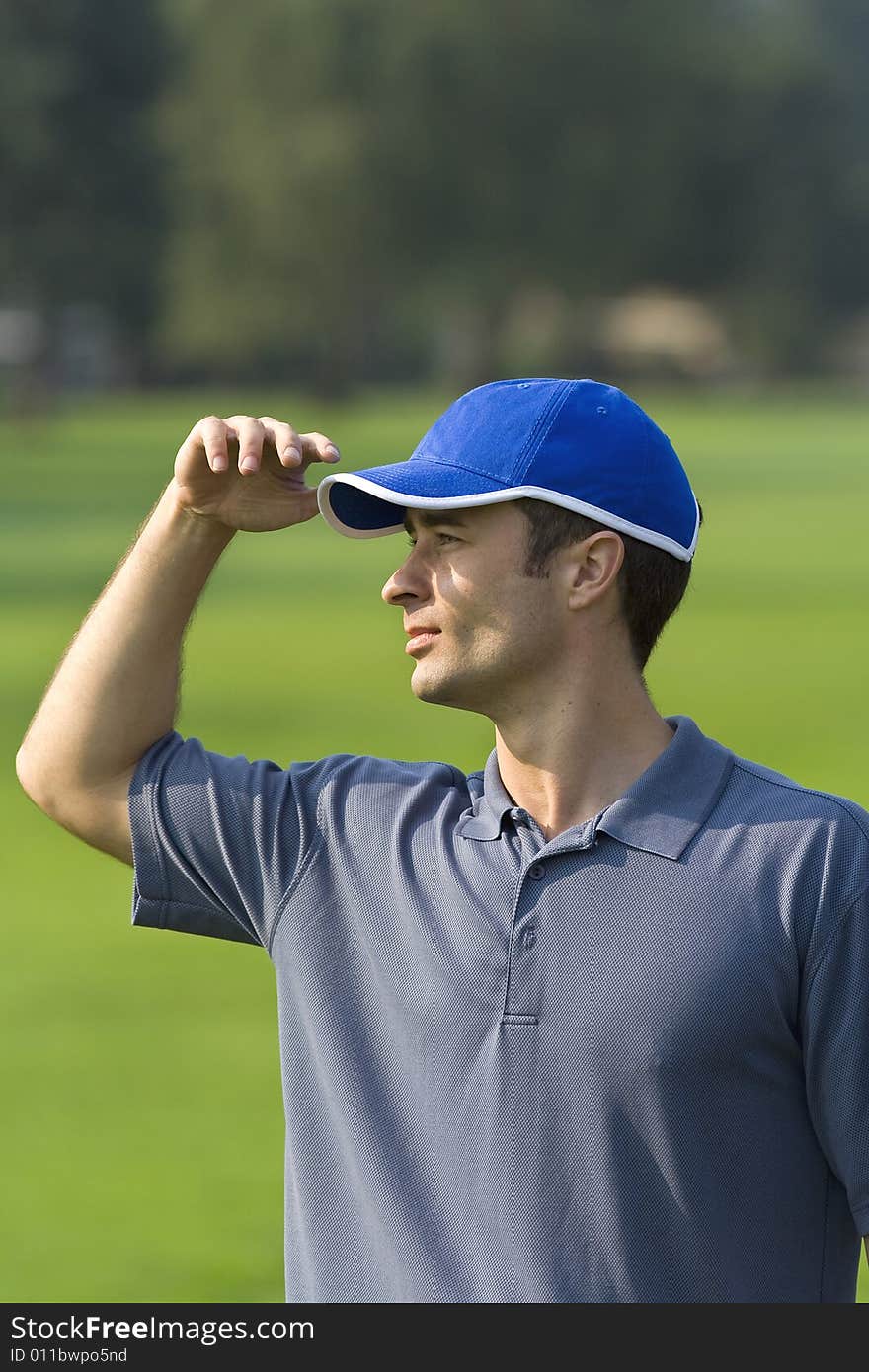 Man's profile while standing on golf course shielding eyes from sun - Vertically framed photo. Man's profile while standing on golf course shielding eyes from sun - Vertically framed photo