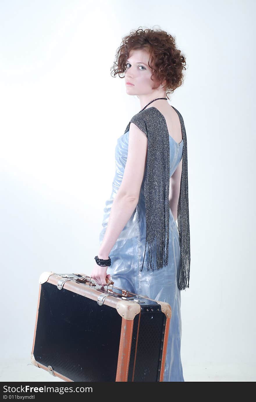 A young girl with a curly hair, dressed in the outmoded clothes, holds an old suitcase in a hand and looks a sorrowful look through a shoulder. A young girl with a curly hair, dressed in the outmoded clothes, holds an old suitcase in a hand and looks a sorrowful look through a shoulder