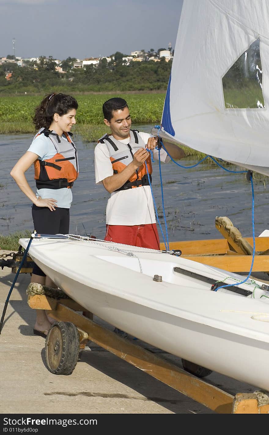 Man teaching woman how to sail with sailboat on trailer. Man showing woman sail rigging. Vertically framed photo. Man teaching woman how to sail with sailboat on trailer. Man showing woman sail rigging. Vertically framed photo