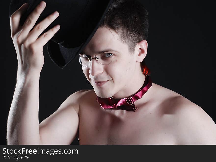 Young man in a black cylinder and tie without a shirt on a black background. Young man in a black cylinder and tie without a shirt on a black background