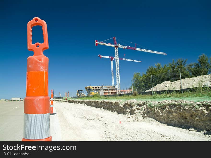 Warning or safety cones designating a construction site with large cranes in the background. Warning or safety cones designating a construction site with large cranes in the background.