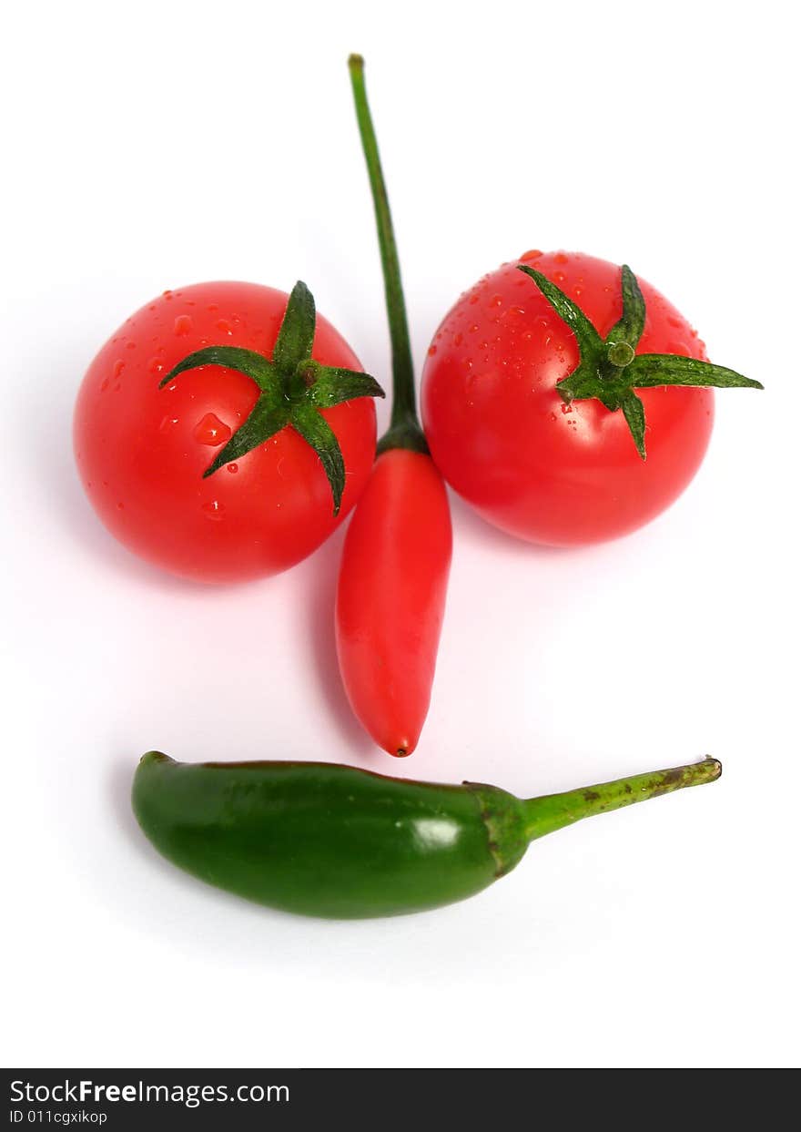 Two colors chilies with cherry tomatoes forming a face on white background. Two colors chilies with cherry tomatoes forming a face on white background