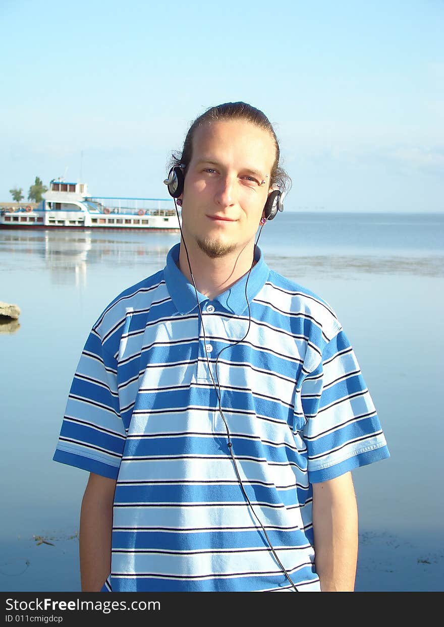 Resting young man with ear-phones on the riverside. Excursion steamship. Resting young man with ear-phones on the riverside. Excursion steamship.