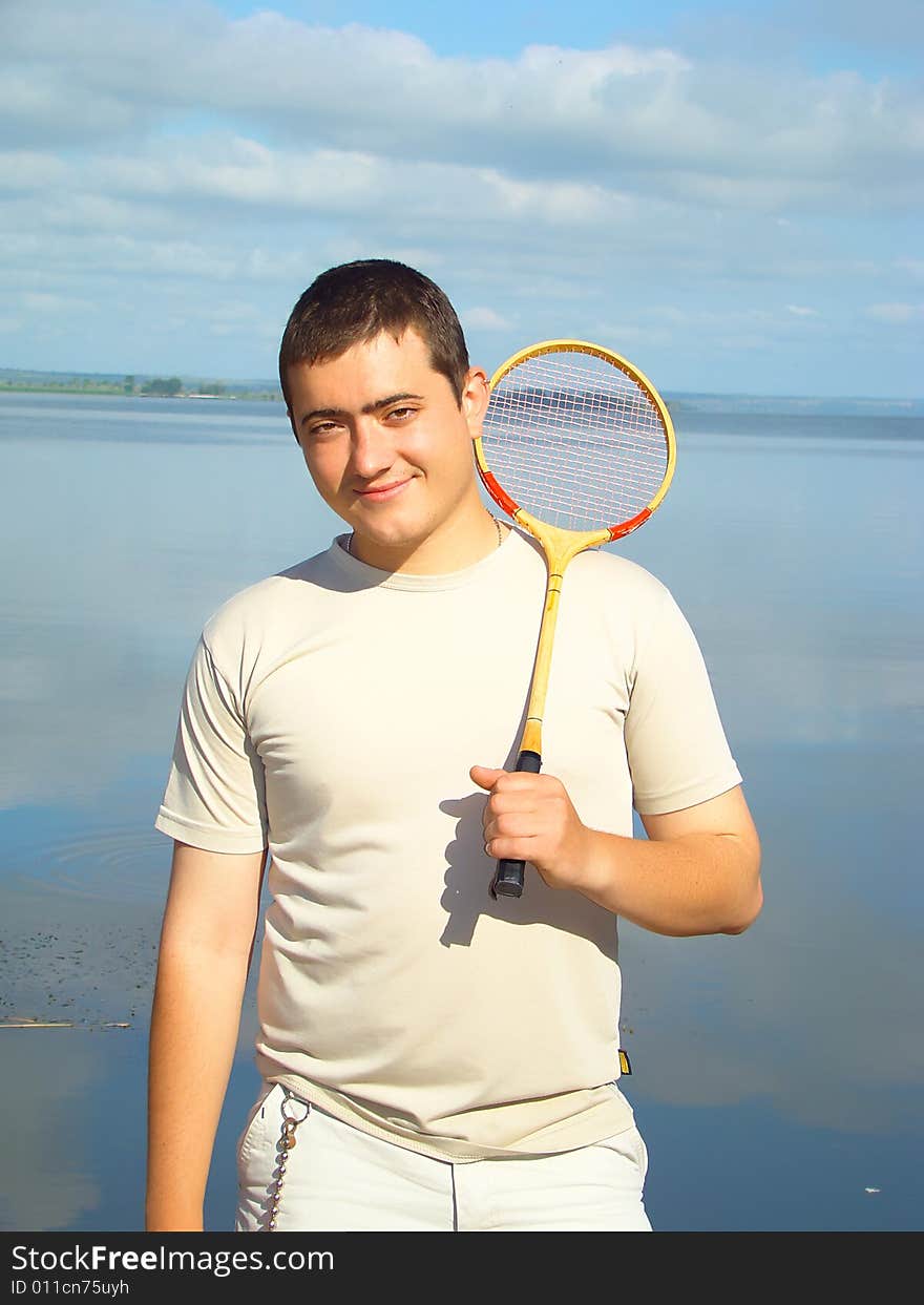 Young man with a racket for a badminton on the riverside.  Sport and rest. Healthy life. Young man with a racket for a badminton on the riverside.  Sport and rest. Healthy life.