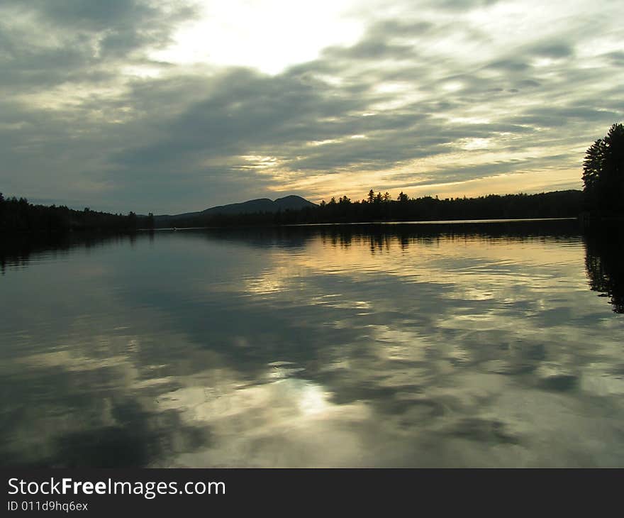 Mountain and trees silhouetted at sunset with clouds reflecting on lake in Adirondacks. Mountain and trees silhouetted at sunset with clouds reflecting on lake in Adirondacks.