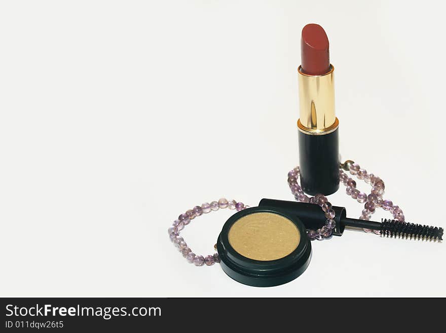 Lipstick, mascara, eyeshadow and a necklace on white background with copy space on left. Lipstick, mascara, eyeshadow and a necklace on white background with copy space on left