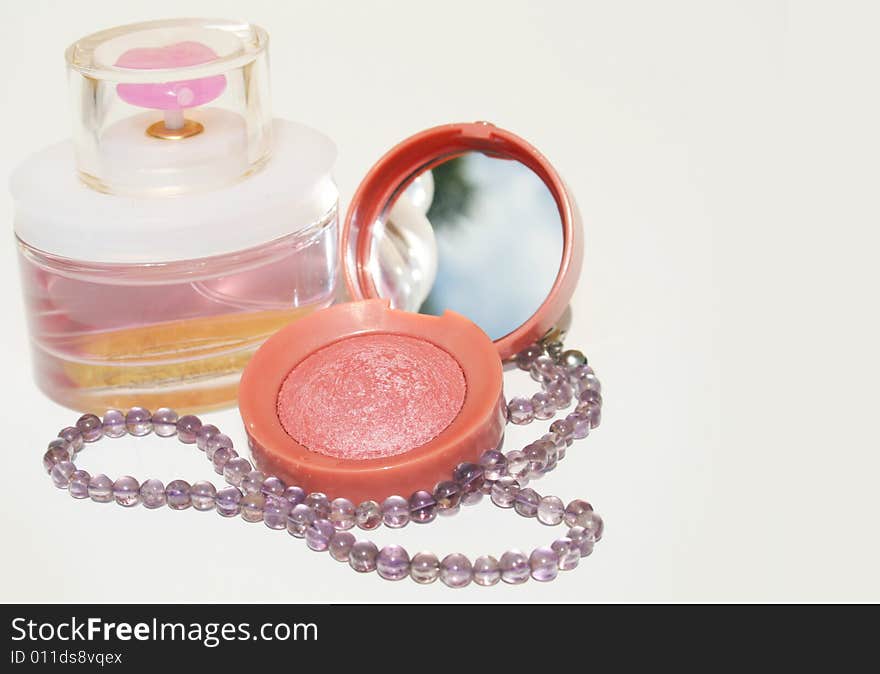 Perfume, blush and a purple beaded necklace on white background with copy space on right. Perfume, blush and a purple beaded necklace on white background with copy space on right