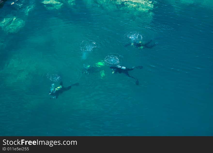 Divers starting to descend in to the blue rocky water. Divers starting to descend in to the blue rocky water