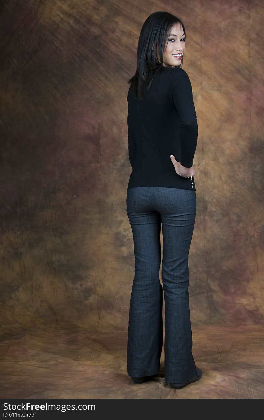 Full length image of a dark haired lady in a blue blouse and denims smiling and looking back with hands on hips. Full length image of a dark haired lady in a blue blouse and denims smiling and looking back with hands on hips.