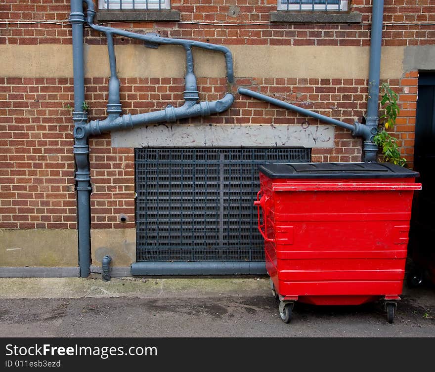 Sewer pipes outside the old brick house and bright red waste container near the wall. Sewer pipes outside the old brick house and bright red waste container near the wall