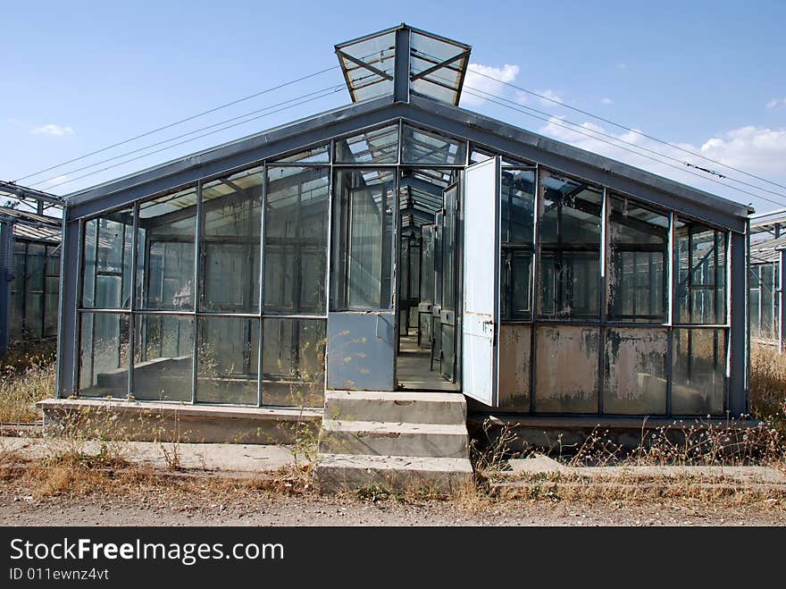 A greenhouse made entirely of glass sits on a green lawn under a blue sky. A greenhouse made entirely of glass sits on a green lawn under a blue sky.