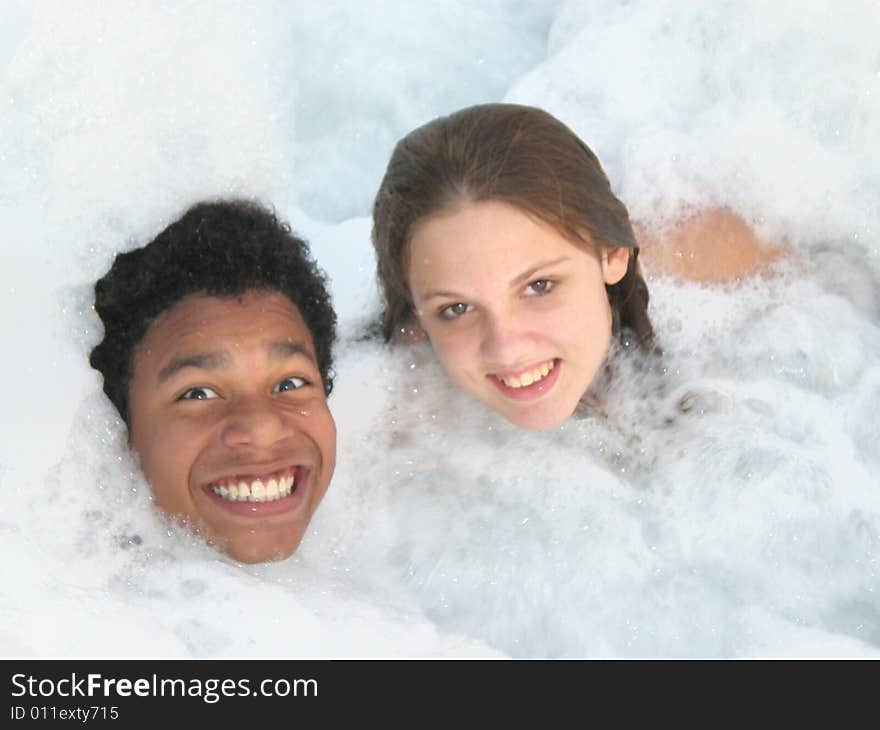 A picture of a black boy and a white girl smiling in a jacuzzi with lots of bubbles. A picture of a black boy and a white girl smiling in a jacuzzi with lots of bubbles.